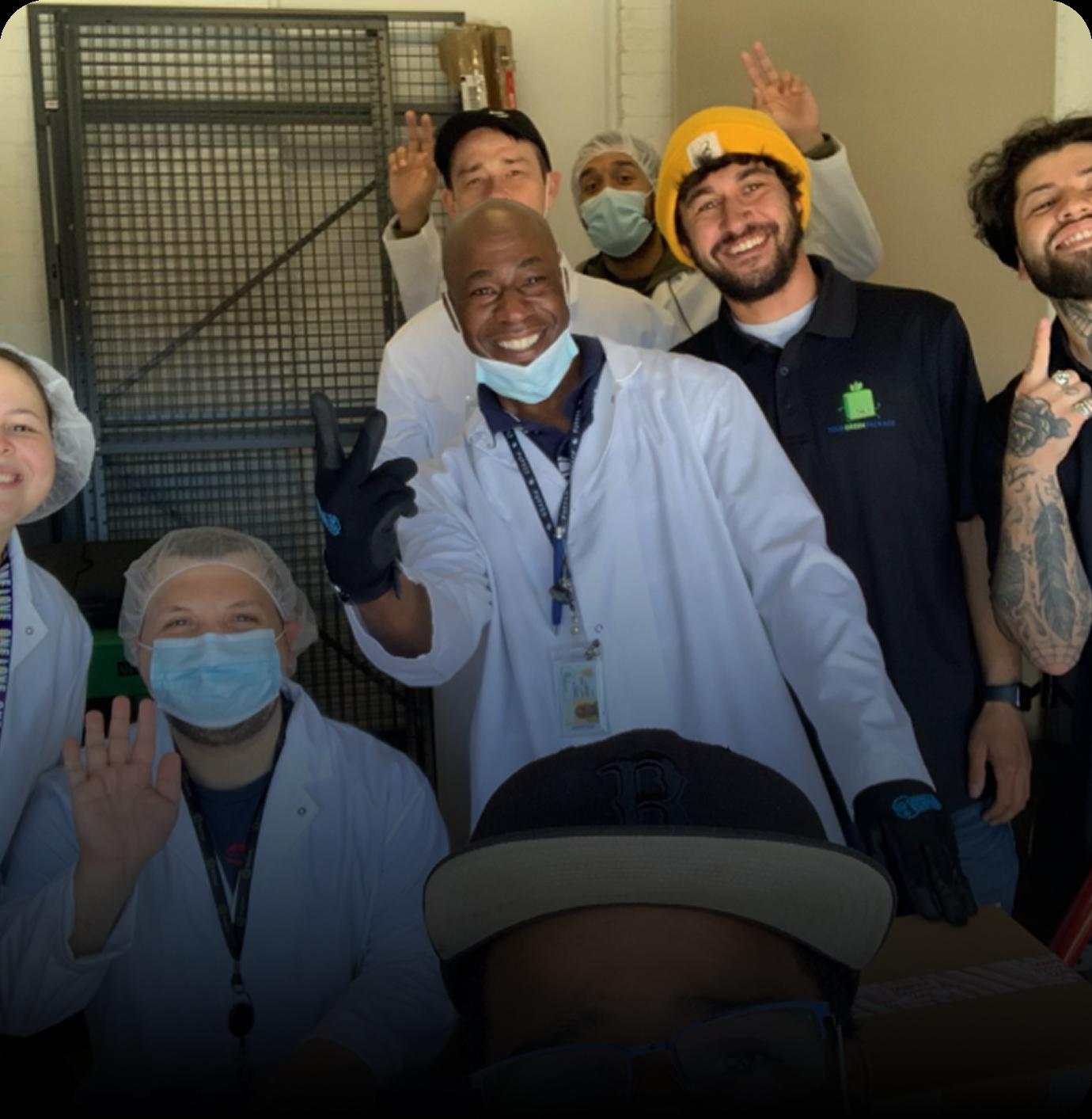 The Your Green Package team in lab coats and gloves inside a warehouse, smiling and posing for a group photo