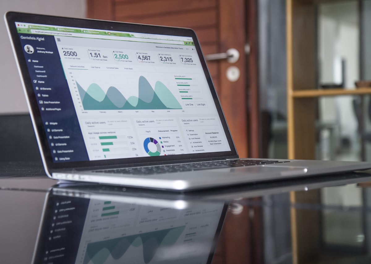 A laptop on a glass table showing a colorful analytics dashboard with charts and linked metrics