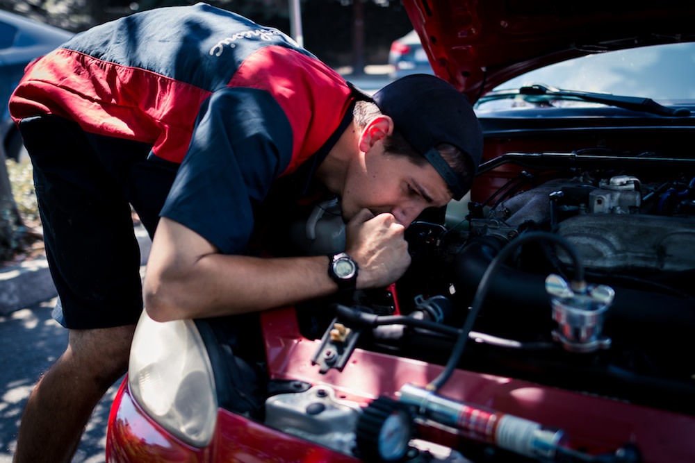 A YourMechanic mobile technician examines the engine of a red car outdoors