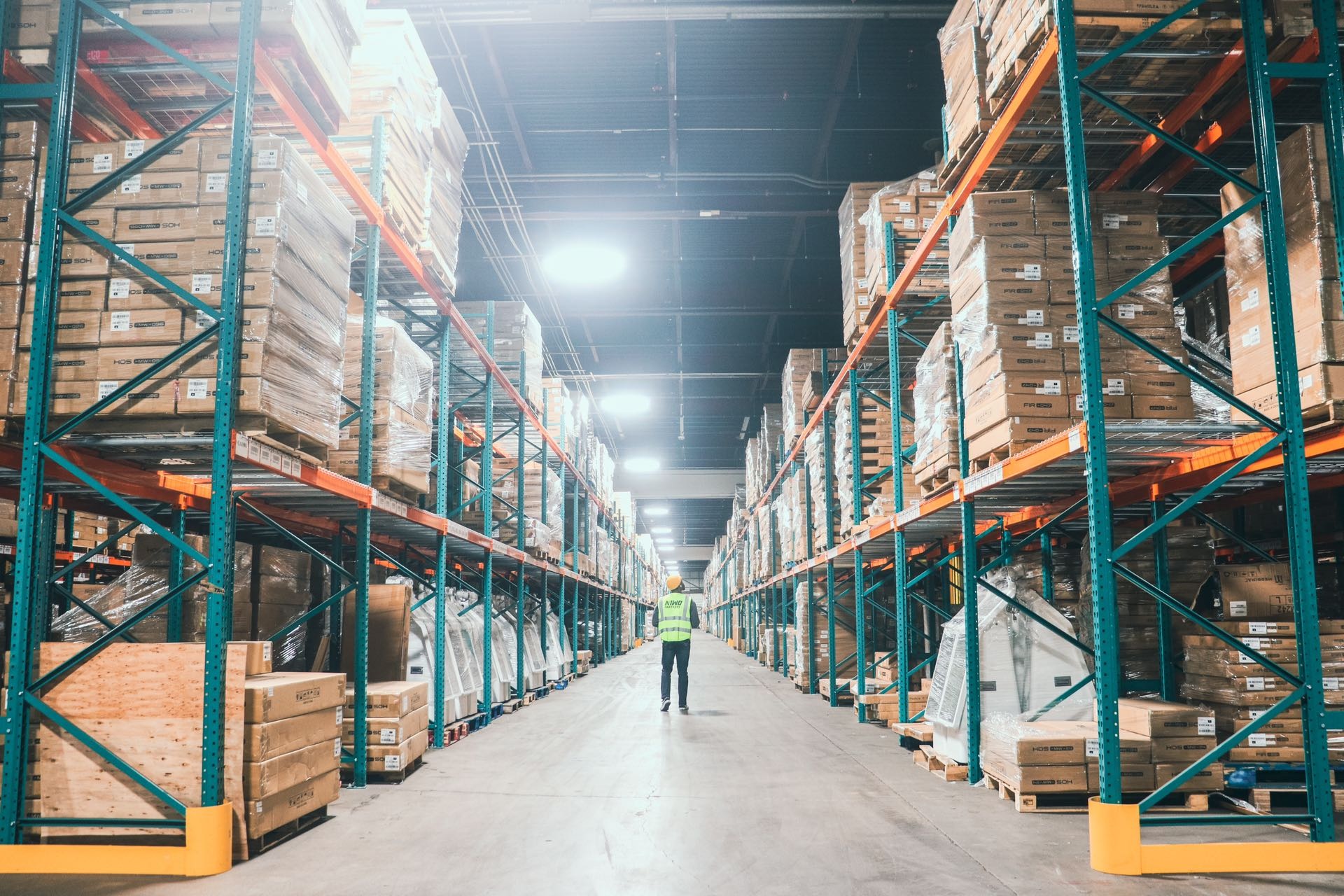 A worker walks between tall racks of boxed goods in a warehouse