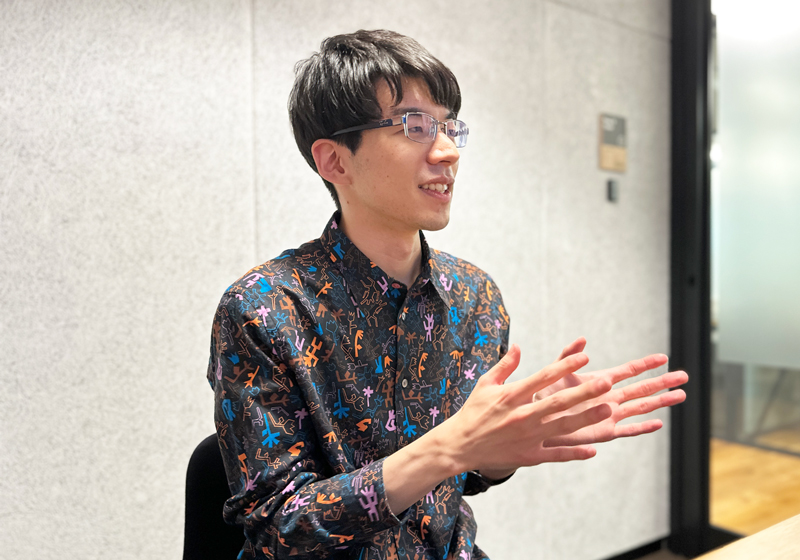 Yuki Kaneko speaking and gesturing at a table during an interview