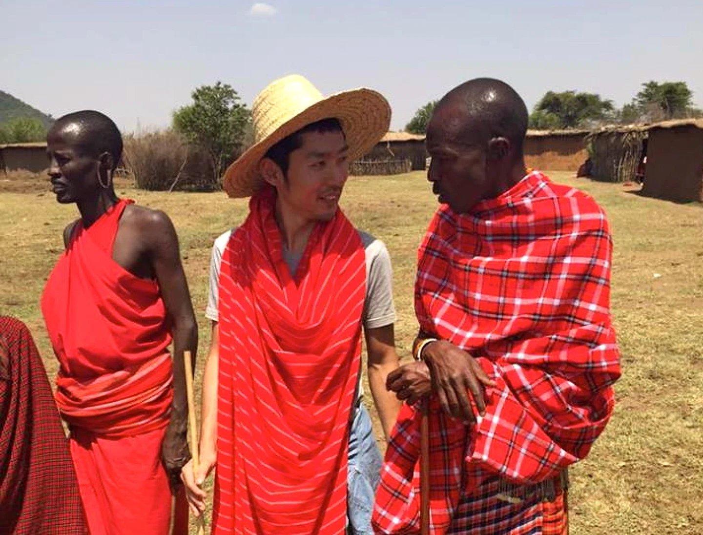 Yuki Mochizuki, wearing a straw hat and red cloth, talking with people during his travels