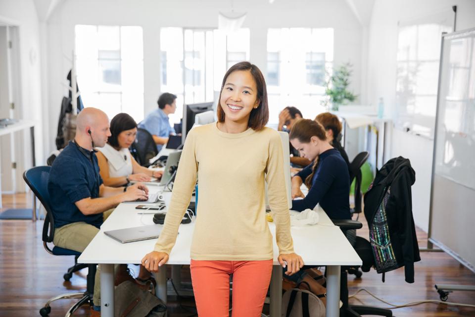 Yunha Kim standing beside a shared office table while colleagues work behind her
