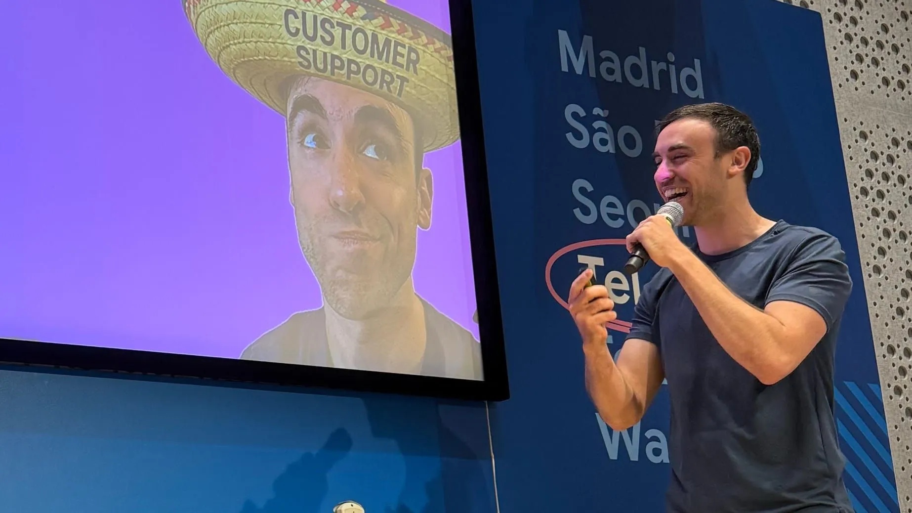 Yuval Karmi speaking into a microphone beside a presentation slide showing a customer support hat