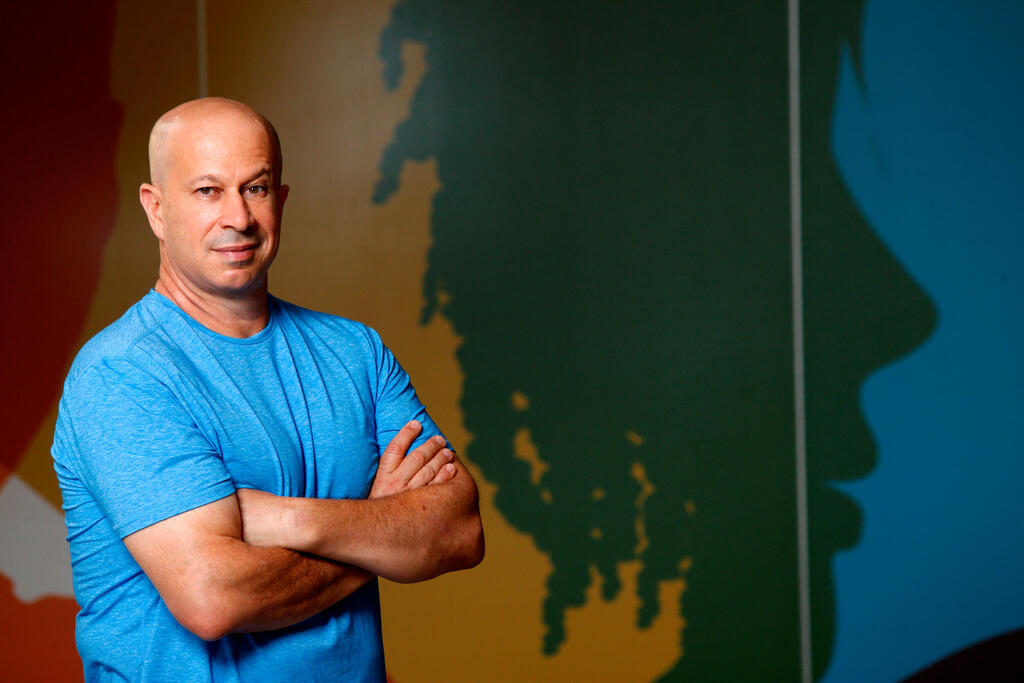 Yuval Tal in a blue shirt standing beside a wall with a world map