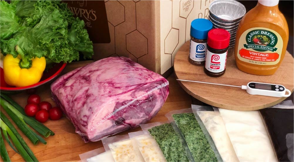 Unboxed Lawry’s At Home shipment with prime rib, sides, seasoning, packaging, and a thermometer