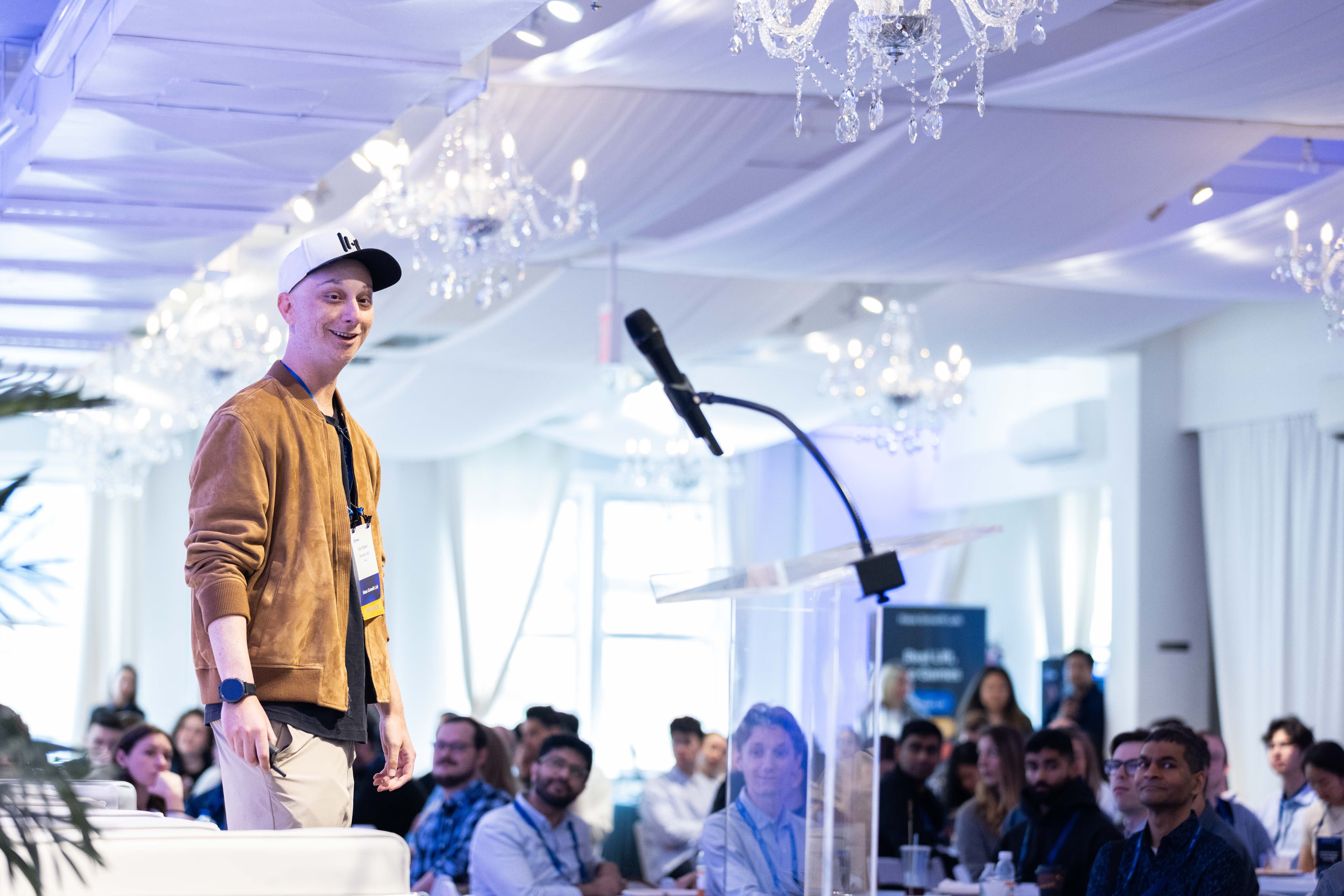 Zach Epstein, wearing a cap and tan jacket, speaking beside a lectern to an audience at Haus Growth Lab in New York