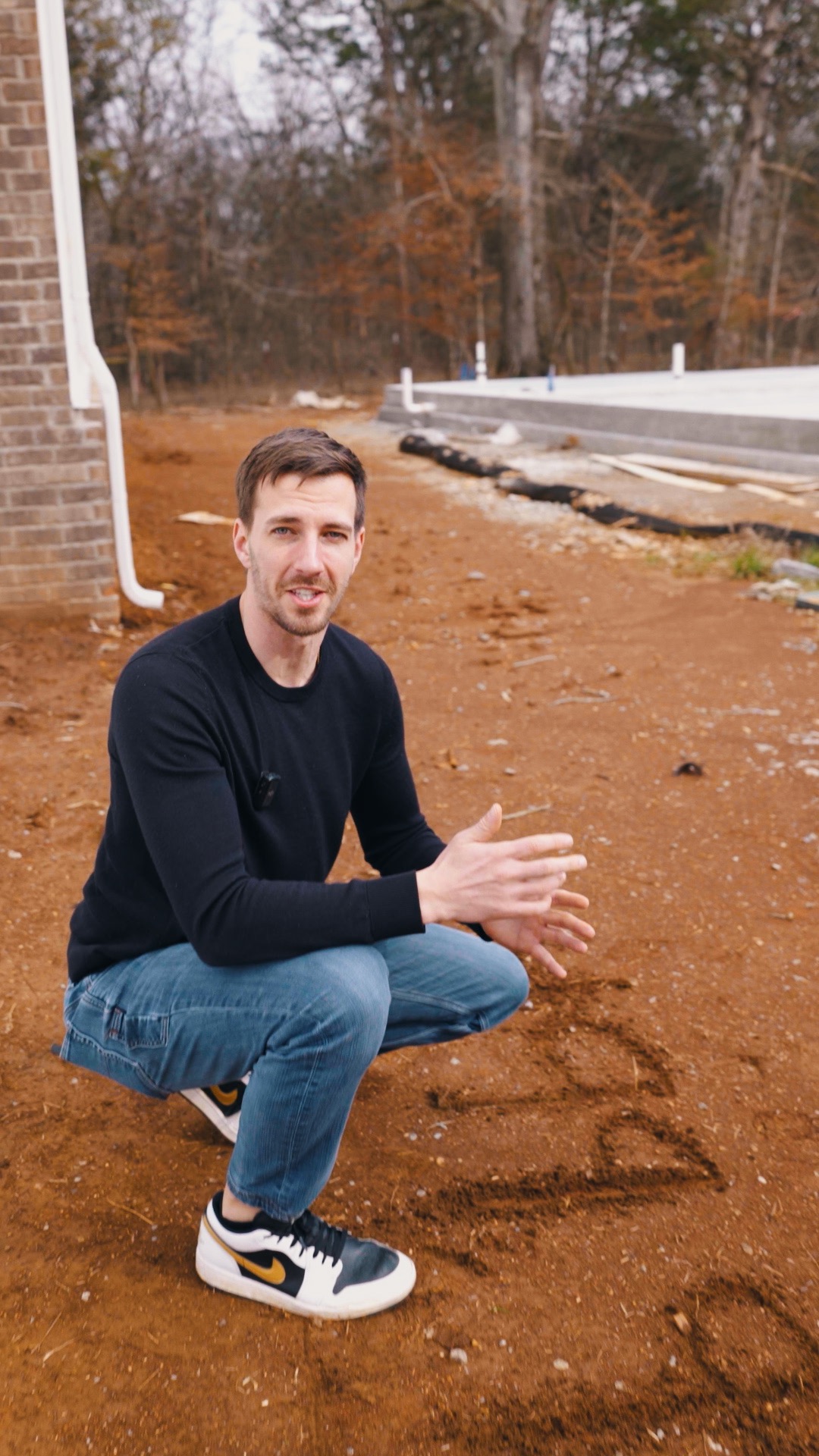 Zach Griest crouches beside a house and a neighboring concrete foundation at a construction site.