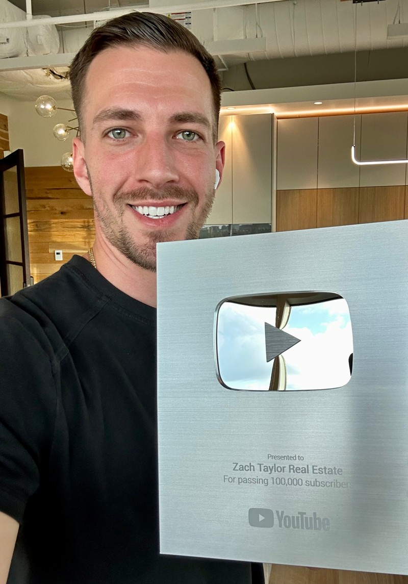 A man holds the silver YouTube creator award presented to Zach Taylor Real Estate for passing 100,000 subscribers