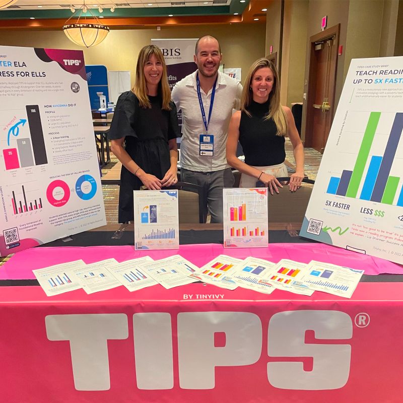 Zachary Silverzweig, center, with two TinyIvy colleagues behind a pink TIPS conference table, surrounded by charts