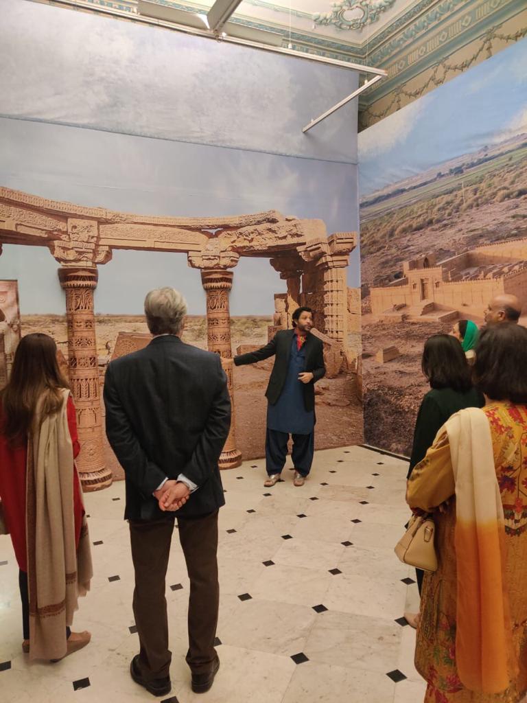Mustafa explaining architectural imagery to a group in a gallery