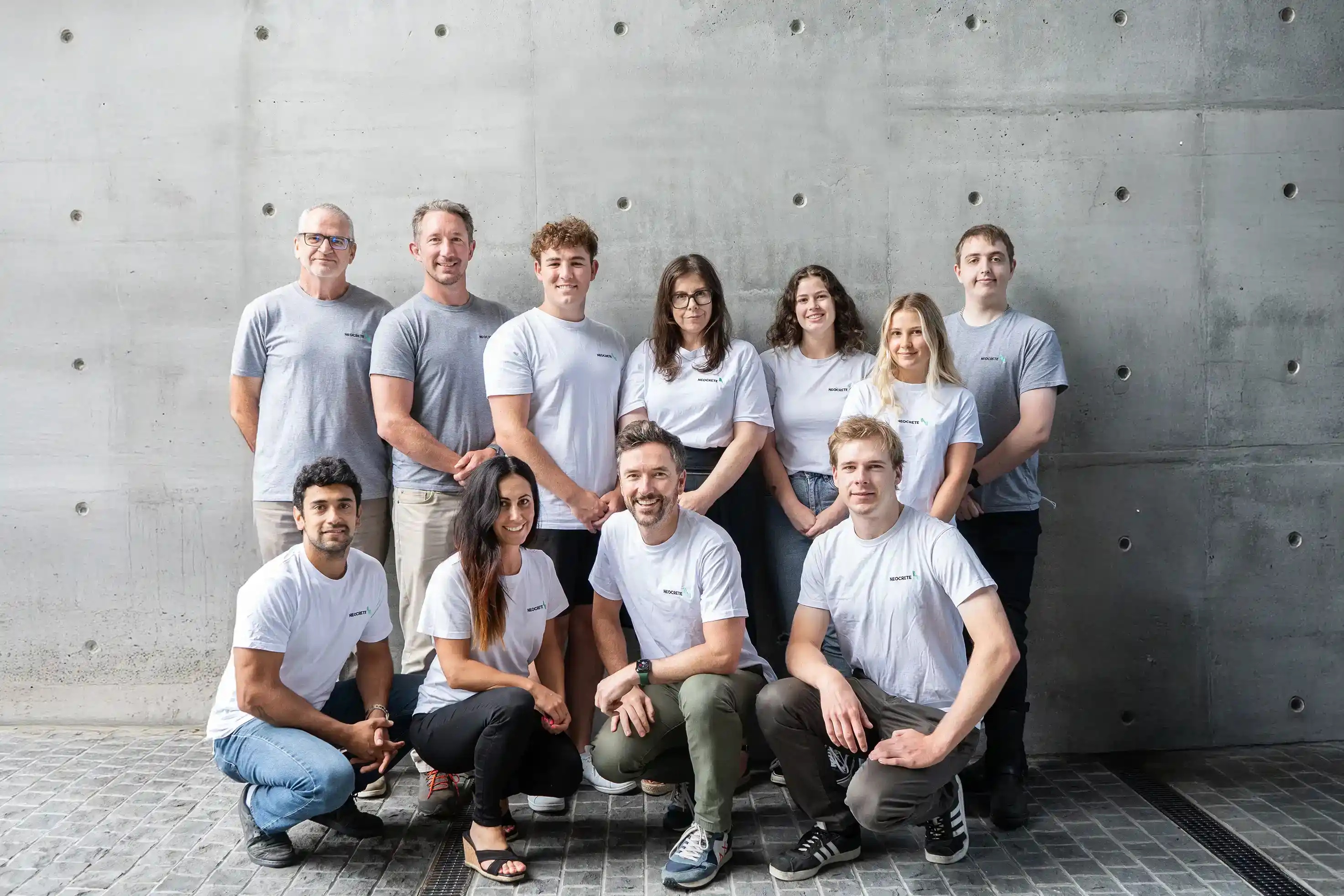 The Neocrete team, including Zarina Alexander seated in the front row, in front of a concrete wall