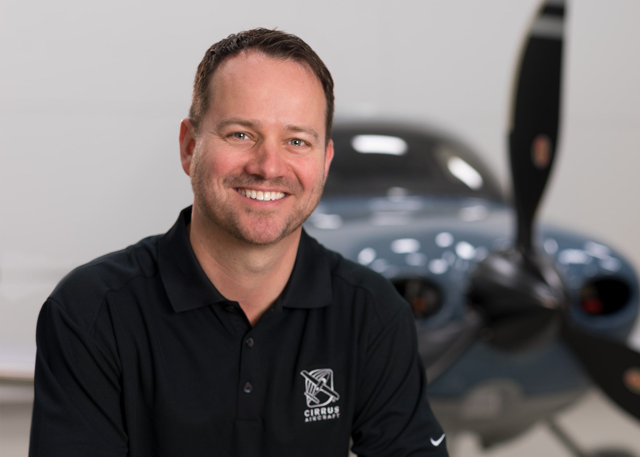 Zean Nielsen in a Cirrus polo shirt with an aircraft behind him