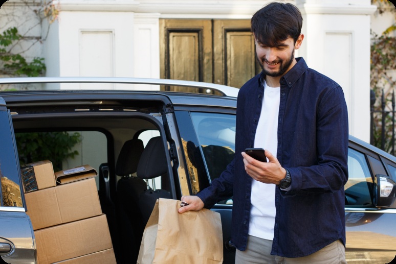 Zego promotional photograph of a driver holding a phone beside a car loaded with delivery parcels
