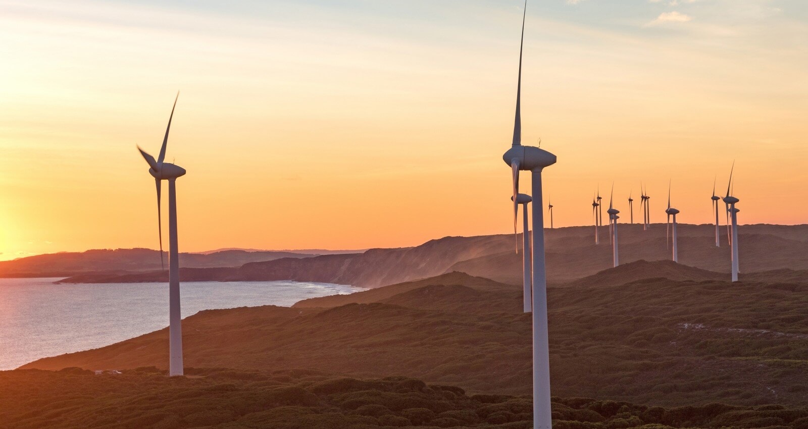 White wind turbines across a coastal landscape at sunset