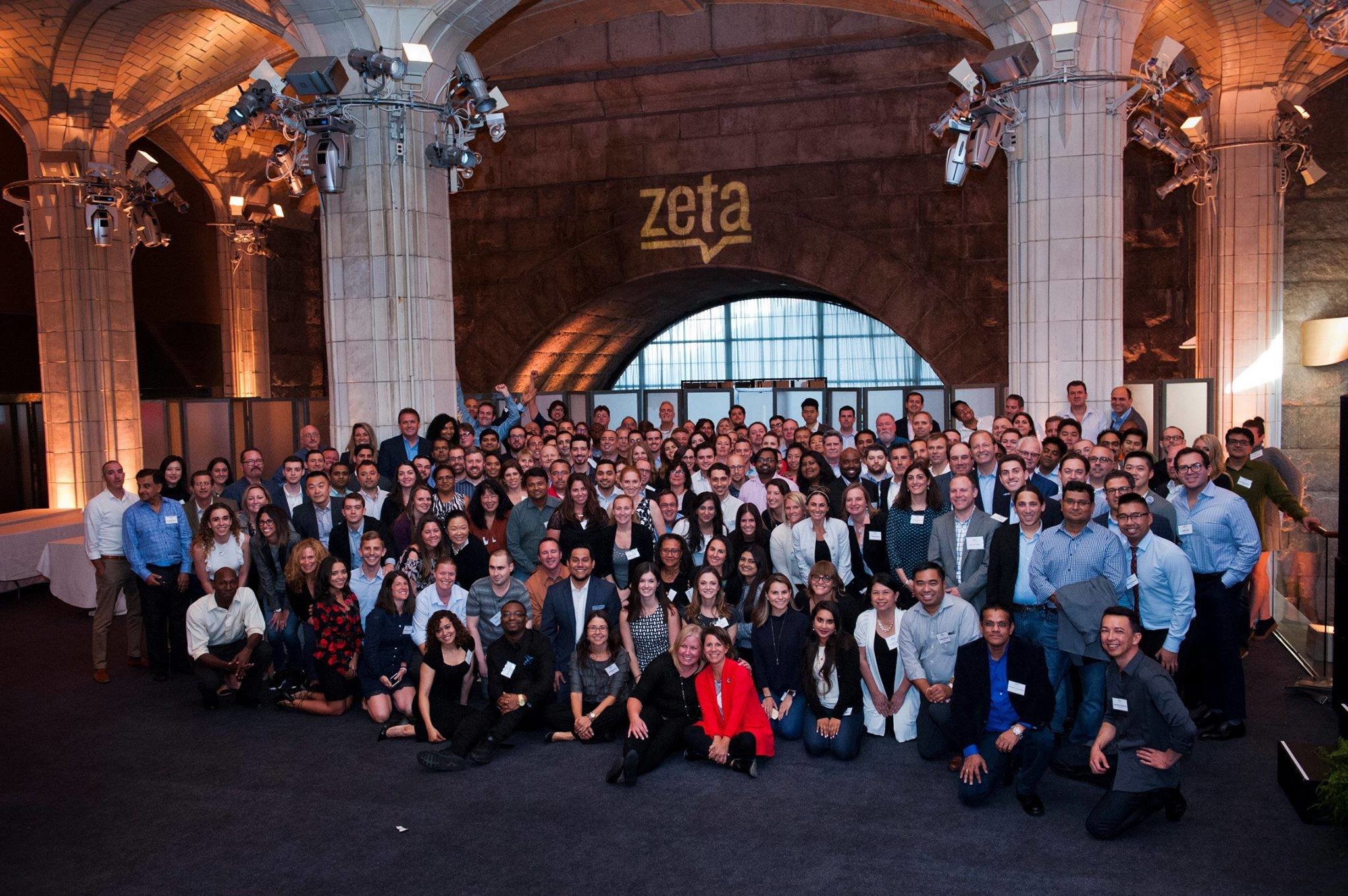 A large group of Zeta Global employees gathered beneath a projected Zeta wordmark