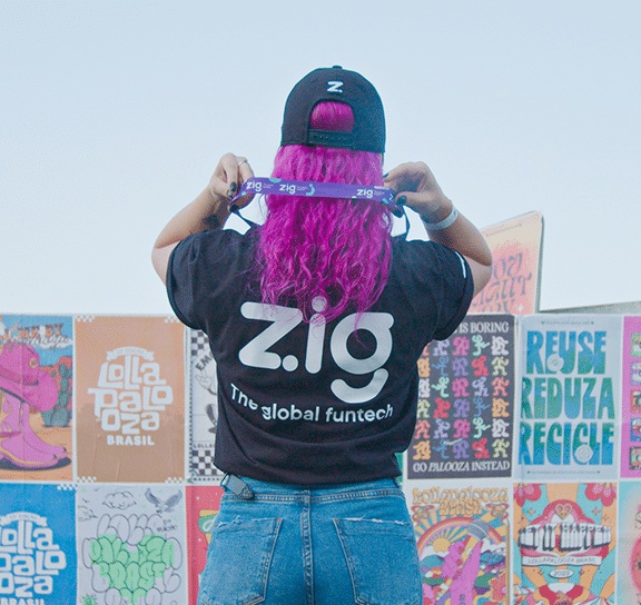 Person in a Zig shirt holding a branded wristband in front of colorful posters