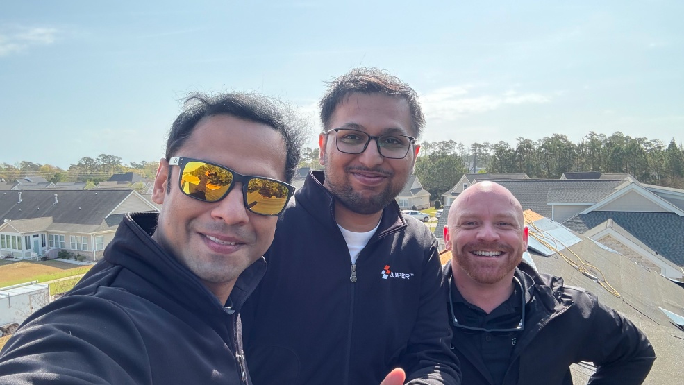 Three people from Zuper’s rooftop visit, with neighborhood rooftops behind them