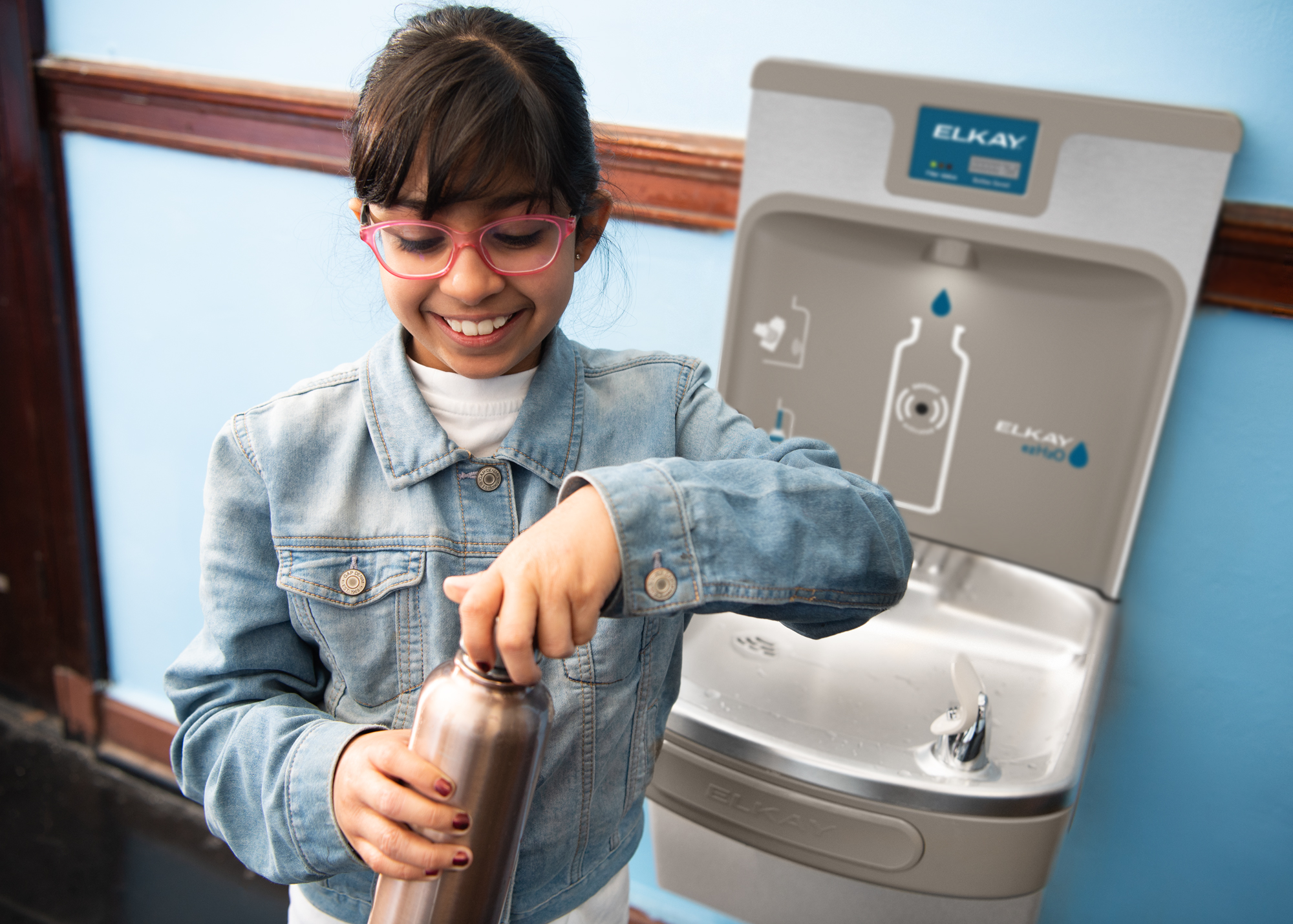 A student closes a reusable bottle beside an Elkay ezH2O bottle filling station